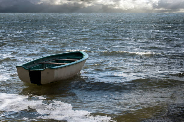 bote vacío flota solitaria sobre las olas del mar a las nubes en el horizonte amplio, con espacio de copia en el agua del paisaje marino - rowboat fotografías e imágenes de stock