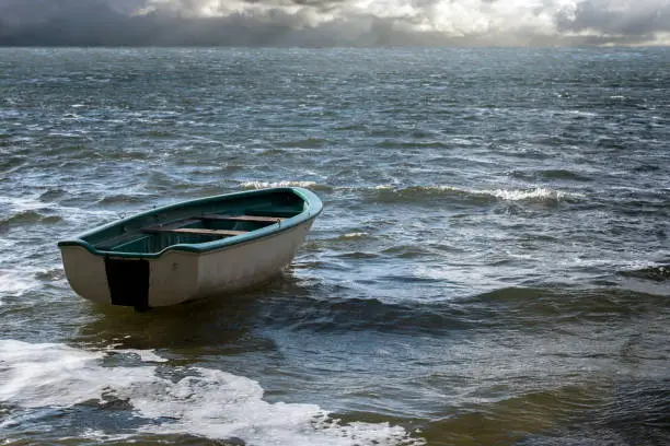 Photo of Empty rowboat floats lonely on the sea waves to the clouds at the wide horizon, seascape with copy space in the water