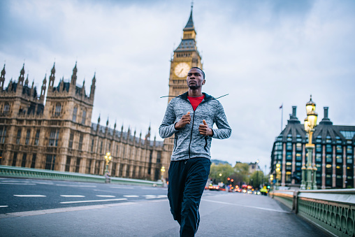 African-American man running outdoors in the city. He is focused and determined. Big ben in the back.