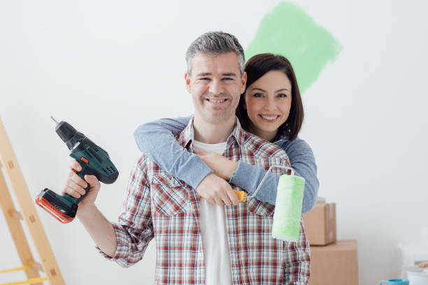 Couple doing home renovations Smiling loving couple doing home renovations, the woman is holding a paint roller and the man is using a drill holding drill stock pictures, royalty-free photos & images