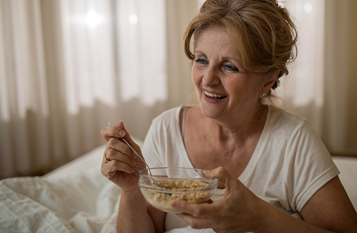 Smiling senior woman eating healthy breakfast in her bedroom.Smiling senior woman eating healthy breakfast in her bedroom.