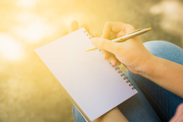 istock Close up of woman's hand writing something down in a notebook empty. While she was sitting in a park / business concept. 671294550