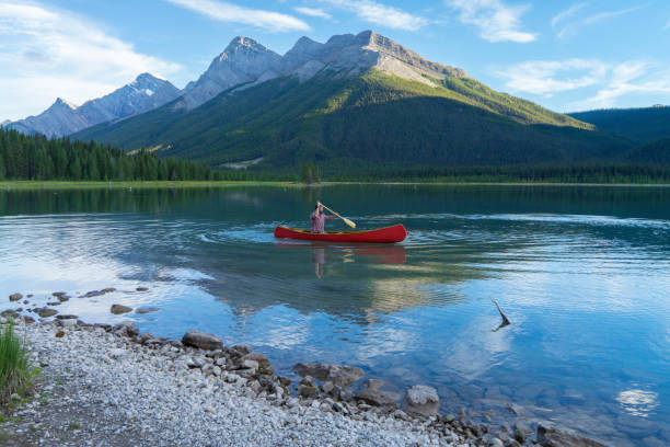 istock Man paddles canoe along mountain lake 671365491