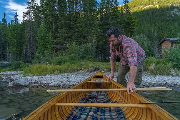 Photo of Man pushes canoe into mountain lake