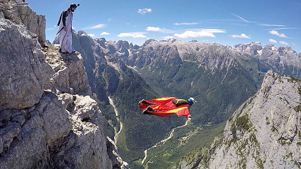 Wingsuit fliers descend from cliff summit stock photo