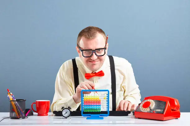 Studio portrait of happy nerd guy with glasses calculating on child abacus. Behind him is blue background