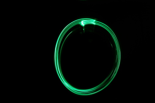 Long exposure photography. A circle shape 'light painted' by green fairy lights, against a clean, black background