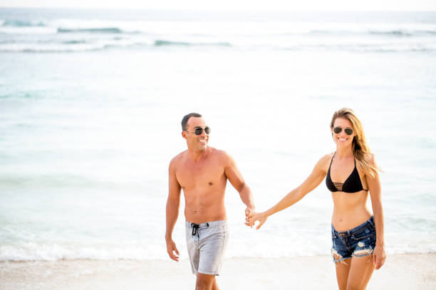 istock Happy young couple walking holding hands on beach 671386398