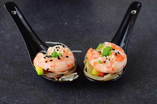 Noodles with prawns and vegetables in traditional soup spoons on a grey abstract background. Healthy food concept
