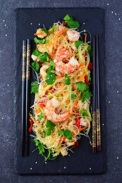 istock Noodles with prawns and vegetables on a black stone plate on a grey abstract background. Healthy food concept 671392448