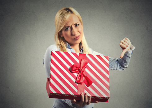 Closeup portrait young woman holding, opening gift box, displeased, disgusted with what she received, isolated on gray background. Negative human emotion, facial expression, feeling attitude reaction