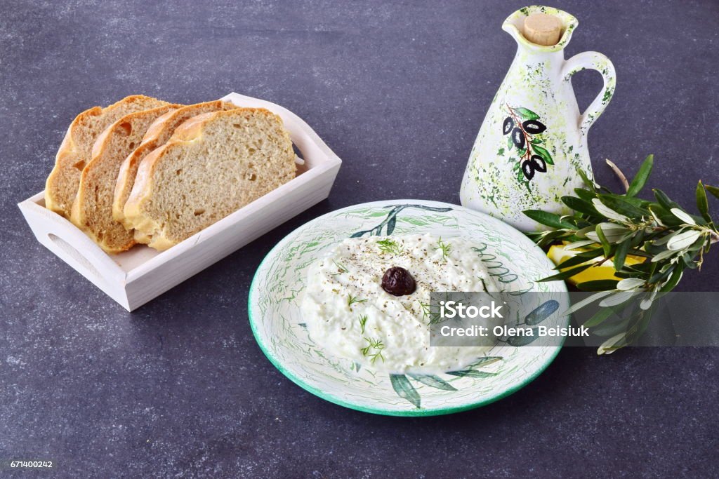 Greek traditional sauce tzatziki with olives, olive oil jar, lemon and bread on a grey abstract background. Healthy eating concept Tzatziki Stock Photo