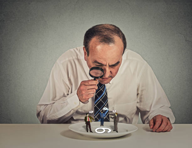 istock Curious corporate businessman skeptically meeting looking at small employee standing on table plate through magnifying glass 671405054