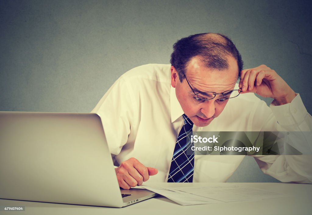 Confused surprised business man looking at documents. Shocked corporate middle aged executive working at his desk in office reviewing paperwork Mistake Stock Photo