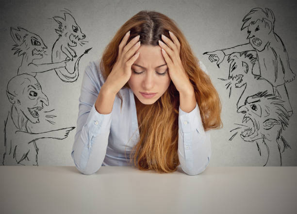 Desperate young businesswoman sitting at desk in her office Evil Men pointing at stressed woman. Desperate young businesswoman sitting at desk in her office isolated on grey wall background. Negative human emotions face expression feelings life perception negative emotion stock pictures, royalty-free photos & images