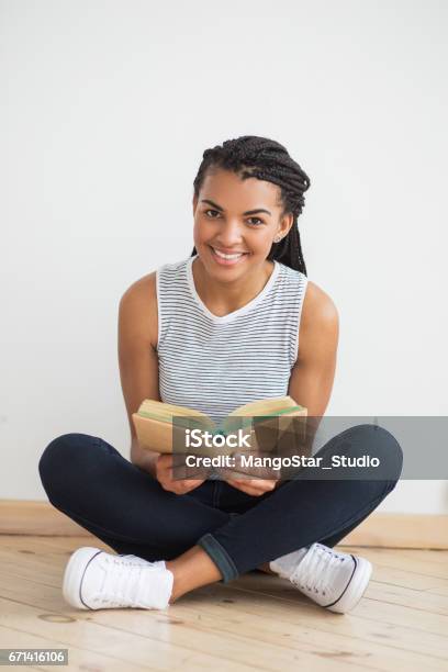 Photo libre de droit de Femme Noire Souriante Assis Sur Le Plancher Avec Livre banque d'images et plus d'images libres de droit de Adulte