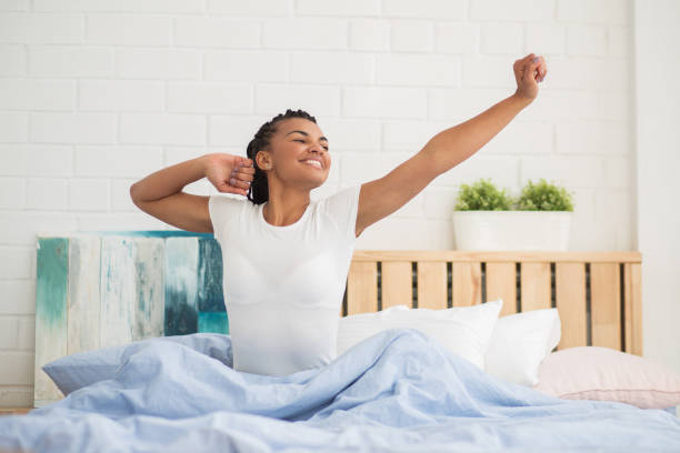 беззаботная женщина растяжения и сидя в постели - waking up women bedding underwear стоковые фото и изображения