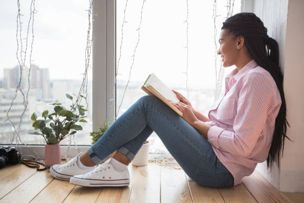 istock Pensive woman with book looking out window 671418252