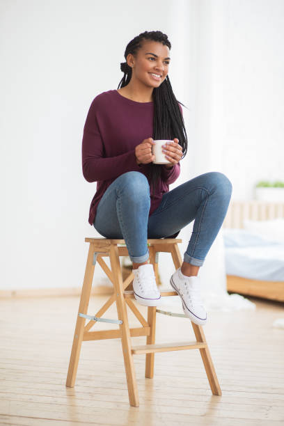 istock Smiling black woman with mug sitting on stool 671418320