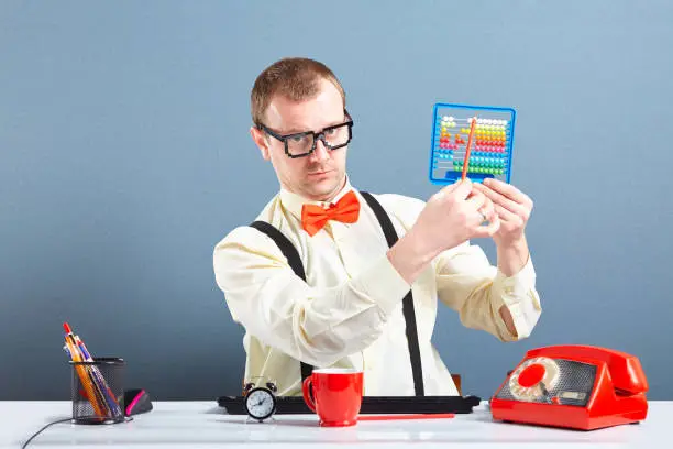 Studio portrait of nerd guy with glasses calculating on child abacus. Behind him is blue background