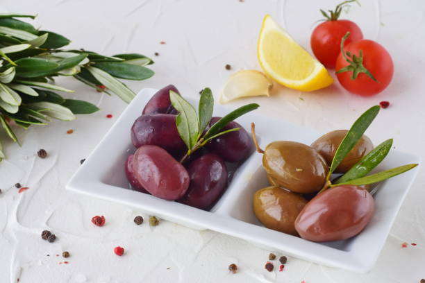 istock White plate with black and green olives with olive leaves on a white abstract background with lemon, cherry tomato, spices. Healthy food. Greek food. Mediterranean food 671431454
