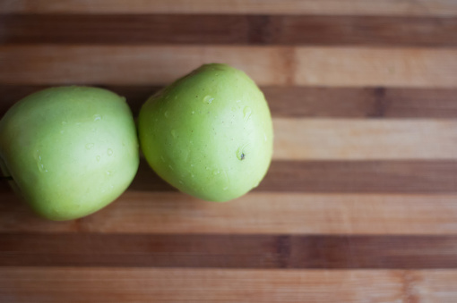 Two green apples lie on wooden cutting board