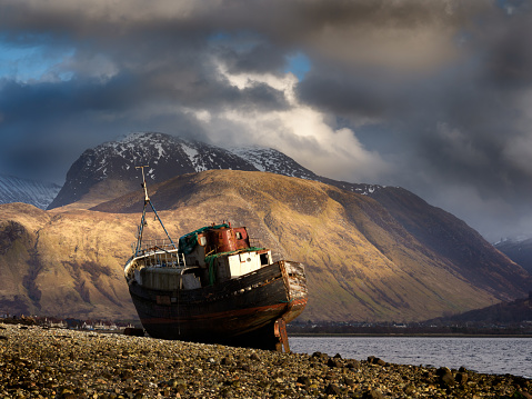 A view towards Ben Nevis from the beach at Corpach, near Fort William in the highlands of Scotland with an old, long abandoned boat resting on the beach.