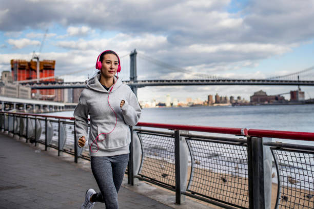 sporty woman jogging on sidewalk by east river - east river audio imagens e fotografias de stock