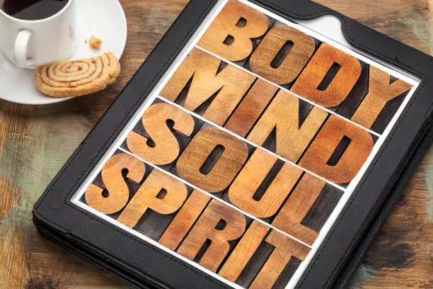 body, mind, soul and spirit - wellness concept - a word abstract in letterpress wood type on a digital tablet with cup of coffee