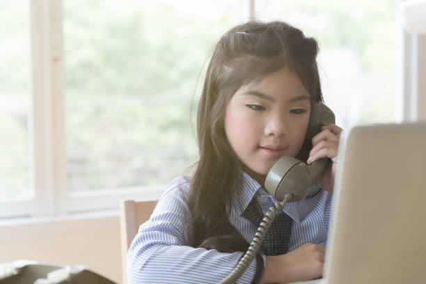 istock asian school girl holding telephone and using laptop computer in a room 671504636