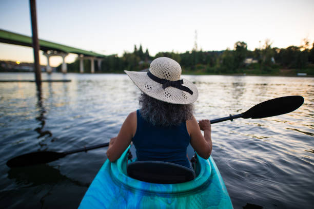 Ethnic female senior citizen kayaks in river on a summer evening