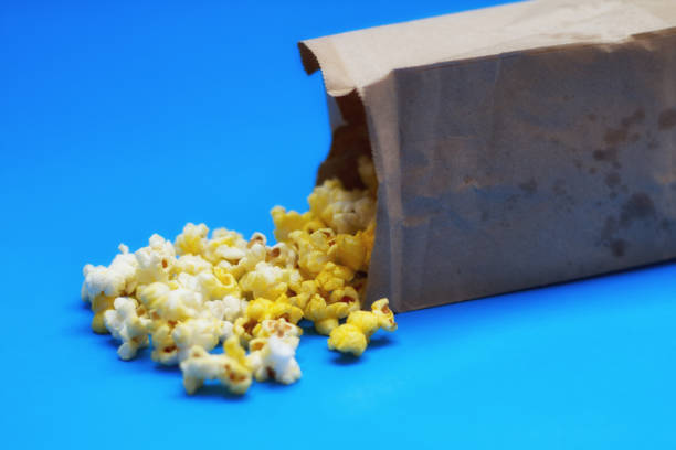 istock Popcorn Spilled from Brown Paper Bag, Blue Background, Close-Up 671515590