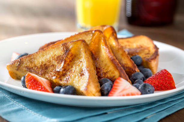 French Toast Morning Light With Syrup and Berries Plate of french toast in the morning light with maple syrup, blueberries, strawberries, and a glass of orange juice on rustic wood table with blue napkin. continental breakfast photos stock pictures, royalty-free photos & images