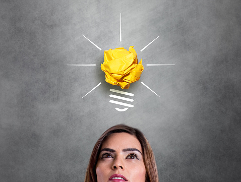 Businesswoman looking at crumpled paper light bulb icon