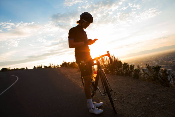 ciclista masculina, verificando o seu celular em uma viagem de treinamento - pedal bicycle sports training cycling - fotografias e filmes do acervo