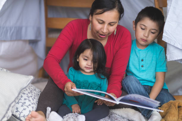Native American mom reads with her two children under makeshift fort in living room Native American mom reads with her two children under makeshift fort in living room fort photos stock pictures, royalty-free photos & images