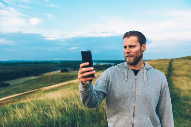 istock Man holds 4G smart phone while standing on a hill in a rural area 671568510