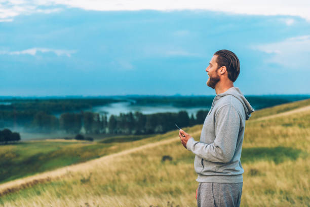 istock Man laughs and holds 4G smart phone while standing on field outside 671568610