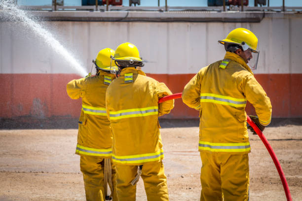 istock Team of fire fighters dousing flames with water from hose 671571420