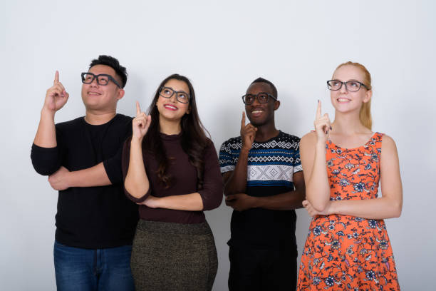 istock Studio shot of happy diverse group of multi ethnic friends smiling and thinking while pointing finger up with eyeglasses together 671571488