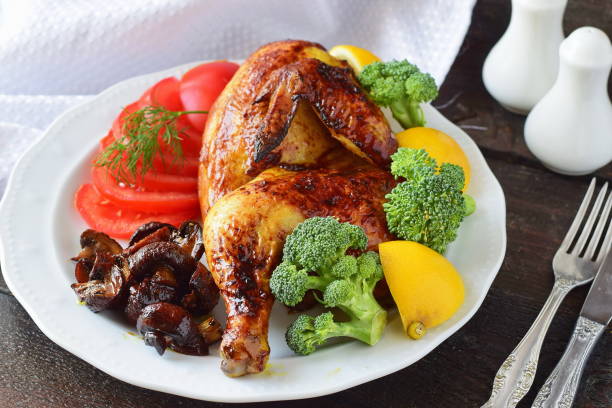 istock Roasted chicken half with boiled broccoli, sliced tomato, lemon and fried mushrooms on a white plate. Ready to serve dish. Cooking step by step. Healthy eating concept 671586690