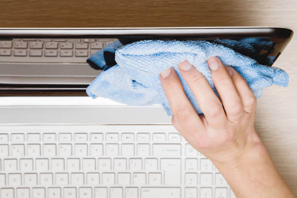 Hand with microfiber cloth carefully wiping laptop screen from dust. Screen shining. Regular clean up.