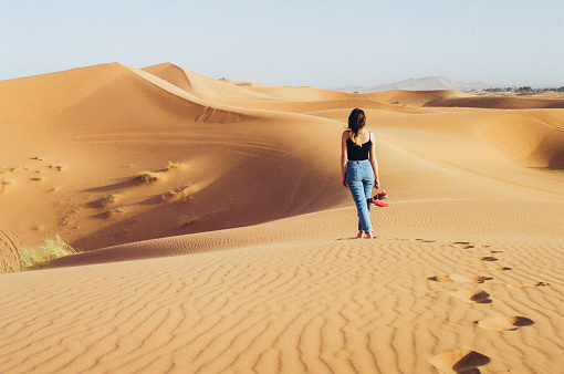 Young Caucasian woman standing barefoot on the dune in the desert, Morocco