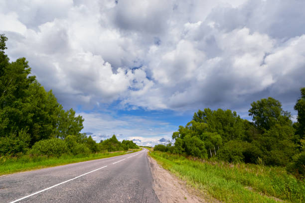 istock Summer road under the clouds, among the trees. 671657160