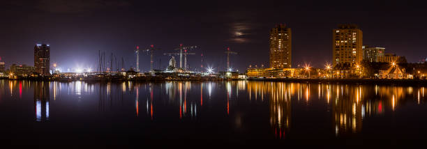 A panorama of the Norfolk and Portsmouth waterfront at night, under a shrouded moon.