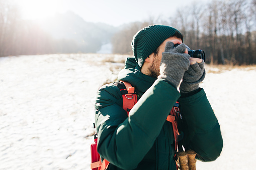 Young hiker exploring nature and photographing winter landscape