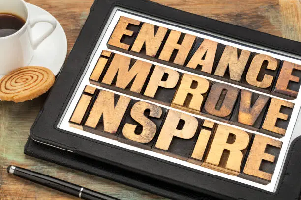 enhance, improve, inspire word abstract  - a collage of motivational words in vintage letterpress wood type on a digital tablet with a cup of coffee