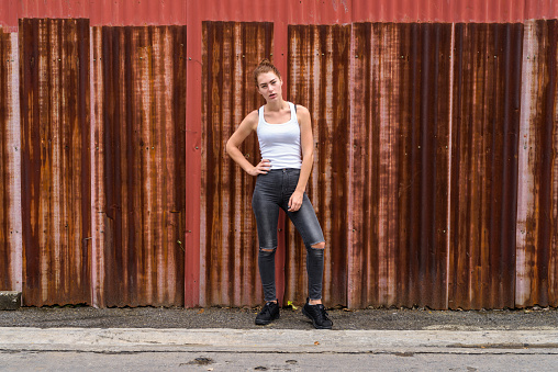 Young beautiful teenage girl standing while posing against old rusty sheet wall horizontal shot