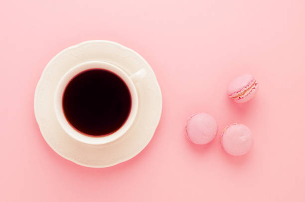 pink macaroons homemade and a cup of coffee on pink background toned, top view