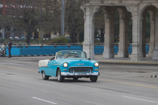 Vintage cars are driving on the street. Incidental people on the background.